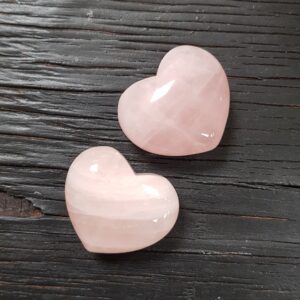 Two Rose Quartz Hearts, pink with some white inclusions, on a dark wooden board