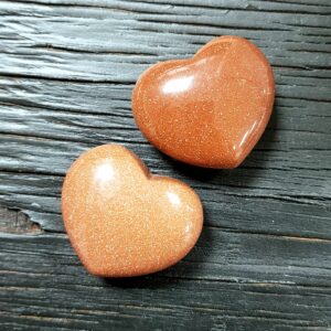 Two Brown Goldstone Hearts, brown with gold flecks, on a black wooden board