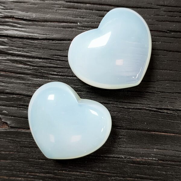 Two Opalite Hearts, translucent pale blues, on a dark wooden board