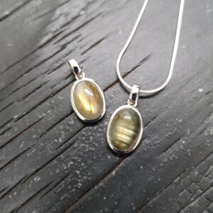 Two labradorite silver frame pendants - oval grey/green with blue and gold flash - in a silver surround, on a dark wooden board