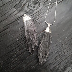 Two Black Kyanite Pendants - black feathery shards with silver bails - on a dark wooden board