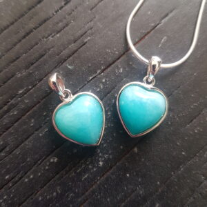 Two Amazonite silver frame pendants - turquoise stone in a heart shape - in a silver surround, on a dark wooden board