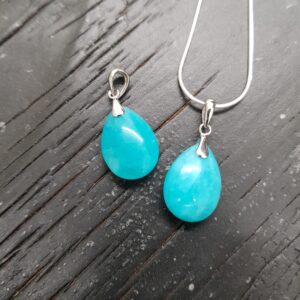 Two Amazonite AA Drop pendants - teardrop shaped teal stone with silver frame and chain - on a dark wooden board