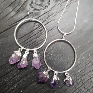 Two Amethyst Ring Pendants - three natural purple amethyst points suspended from a silver hoop - on a dark wooden board