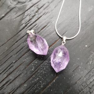 Two Amethyst pendants - light purple stones cut into a faceted shape - on a dark wooden board