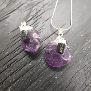 Two Amethyst Tumbestone Pendants - purple round stones with a piece of rough black tourmaline, set in silver - on a dark wooden background