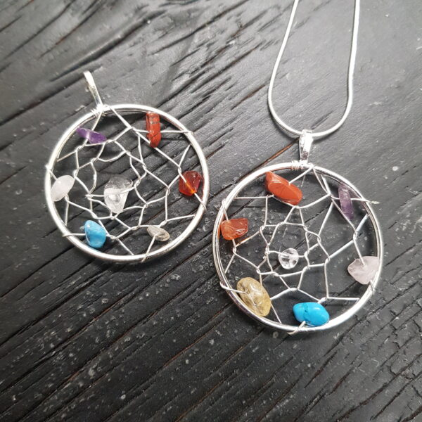Two Dreamcatcher Pendants - silver nets in a circular frame with various stones woven through - on a dark wooden board