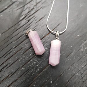 Two Kunzite Tritube pendants - three sides tube with rounded edges in a pale pink stone - on a silver chain, on a dark wooden board