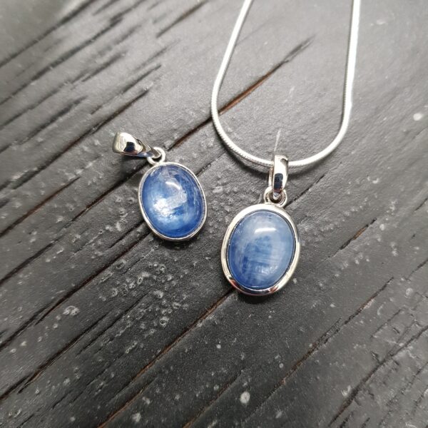 Two Blue Kyanite silver frame pendants - oval blue stone - in a silver surround, on a dark wooden board