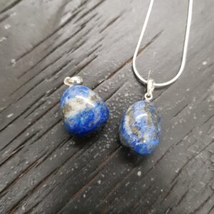 Two Lapis pendants - blue with gold banding - on a silver chain, on a dark wooden board