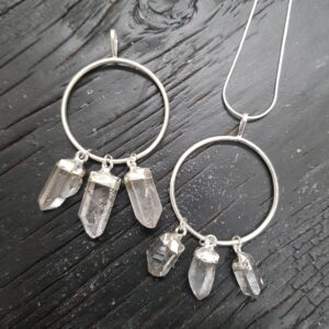 Two Clear Quartz Ring Pendants - three clear natural points suspended from the outside of a silver hoop - on a dark wooden board