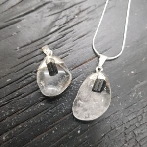 Two Quartz Tumbestone Pendants - clear round stones with a piece of rough black tourmaline, set in silver - on a dark wooden background