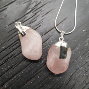 Two Rose Quartz Tumbestone Pendants - pink round stones with a piece of rough black tourmaline, set in silver - on a dark wooden background