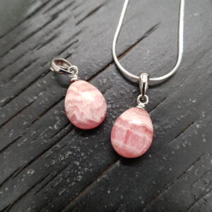 Two Rhodochrosite A- Drop pendants - teardrop shaped banded pink stone with silver frame and chain - on a dark wooden board