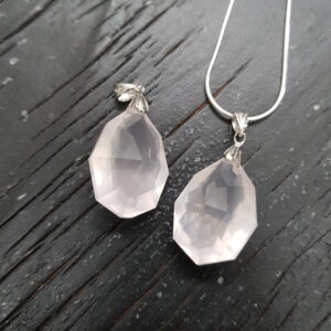 Two Rose Quartz faceted pendants - pale pink stone with cut into many facets - on a dark wooden board