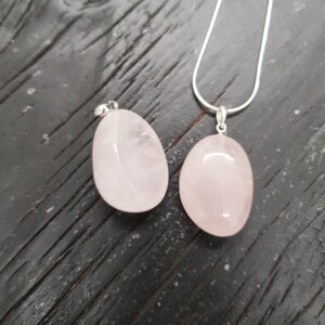 Two Rose Quartz pendants - pale pink with thick white veining - on a silver chain, on a dark wooden board