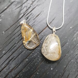 Two Rutilated Quartz pendants - translucent with golden threads - on a silver chain, on a dark wooden board