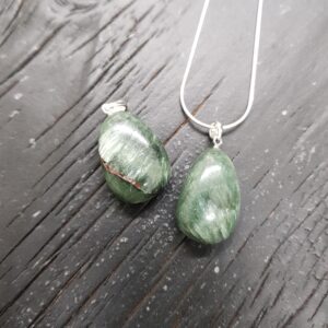 Two Seraphinite pendants - green with light and dark areas - on a silver chain, on a dark wooden board