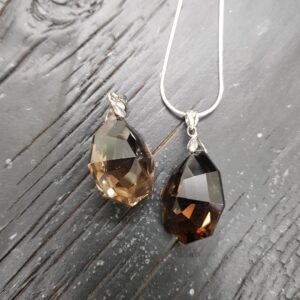 Two Smoky Quartz faceted pendants - dark, transparent stone with cut into many facets - on a dark wooden board