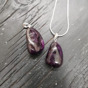 Two Sugilite pendants - dark purple - on a silver chain, on a dark wooden board
