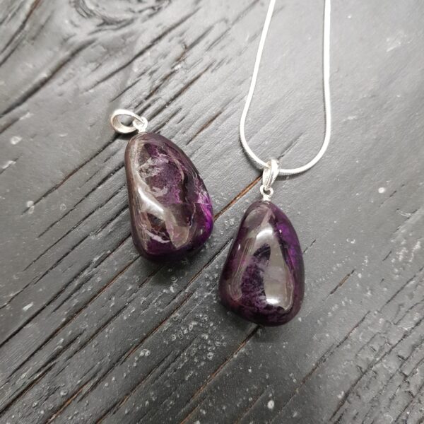 Two Sugilite pendants - dark purple - on a silver chain, on a dark wooden board