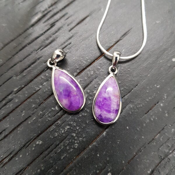 Two Sugilite A+ Drop pendants - teardrop shaped purple stone with silver frame and chain - on a dark wooden board