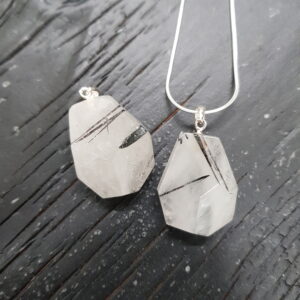Two Tourmalinated Quartz faceted pendants - white with black markings stone with cut into many facets - on a dark wooden board