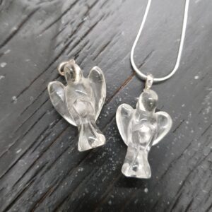 Two clear quartz angel pendants - clear stone with silver tops and chain - on a dark wooden board