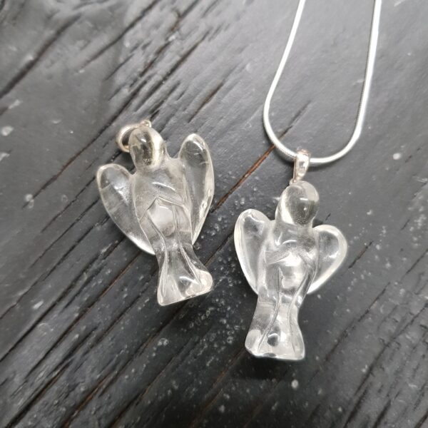 Two clear quartz angel pendants - clear stone with silver tops and chain - on a dark wooden board