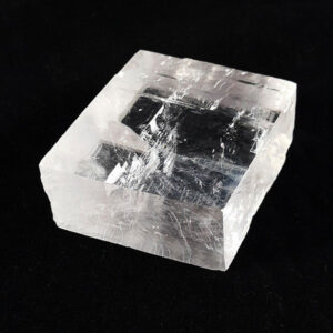 A single piece of Optical Calcite (flat, rectangular shape with a colourless transparency) on a black background