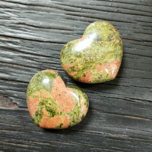 Two Unakite Hearts, green with pink clouds, on a dark wooden board