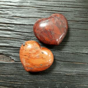 Two Brecciated Jasper Hearts, red with black and white veins, on a dark wooden board