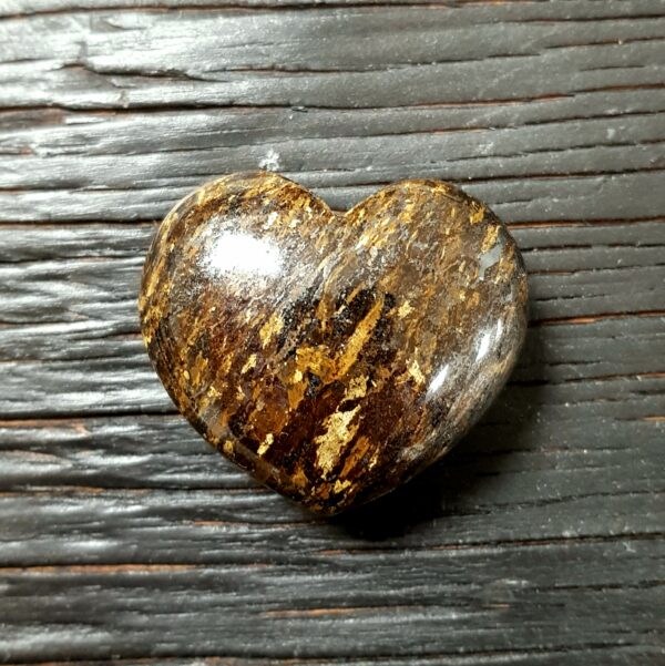 Bronzite Heart, flecks of yellow, brown and gold, on a dark wooden board