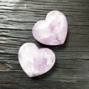 Two Lavender Amethyst Hearts, translucent pale purple, on a black wooden board