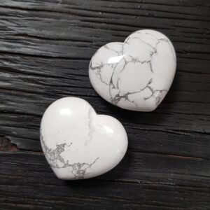 Two Howlite hearts, white with grey marbling, on a black wooden board