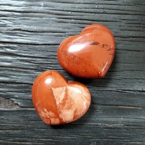 Two Red Jasper hearts, red with pale markings, on a black wooden board