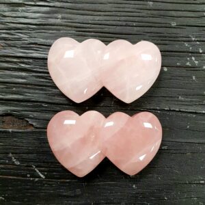 Two Rose Quartz Double Hearts, pink with some white inclusions, on a dark wooden board