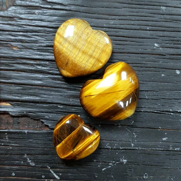 Golden Tiger Eye heart selection, gold and black banding in 4 descending sizes, on a black wooden board