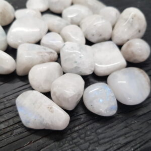 Close up of Rainbow Moonstone - white stone with some blue flash - on a dark wooden board