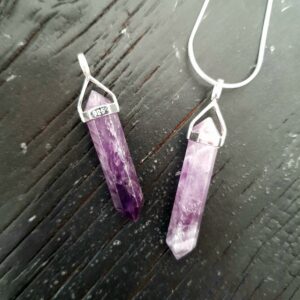 Two Amethyst Double Terminated points (purple facets with points at both ends), on a silver chain, on a dark wooden board