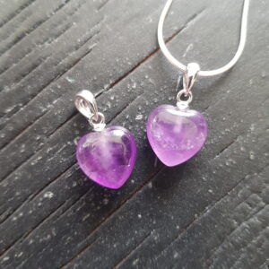 Two Amethyst A+ heart pendants - purple stone cut into a heart shape on a silver chain - on a dark wooden board