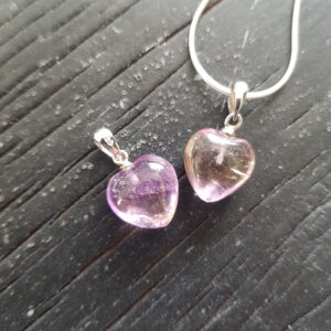 Two Ametrine heart pendants - translucent purple and orange stone cut into a heart shape on a silver chain - on a dark wooden board