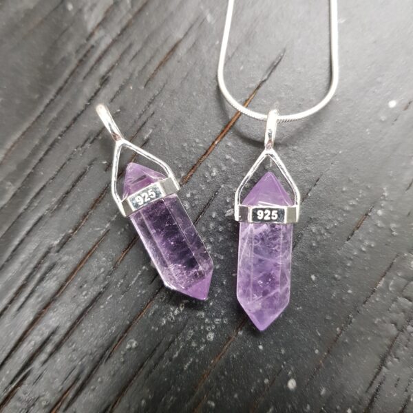 Two Amethyst A Grade Double Terminated points (purple facets with points at both ends), on a silver chain, on a dark wooden board