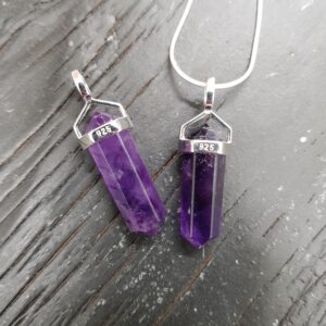 Two Dark Amethyst A Grade Double Terminated points (purple facets with points at both ends), on a silver chain, on a dark wooden board