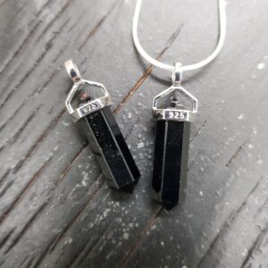 Two Black Tourmaline A/A+ Grade Double Terminated points (black facets with points at both ends), on a silver chain, on a dark wooden board