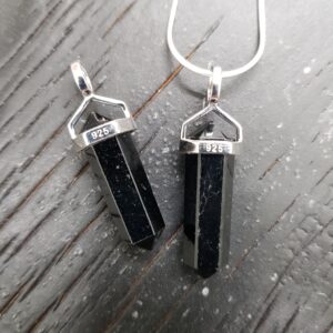 Two Black Tourmaline A+ Grade Double Terminated points (black facets with points at both ends), on a silver chain, on a dark wooden board