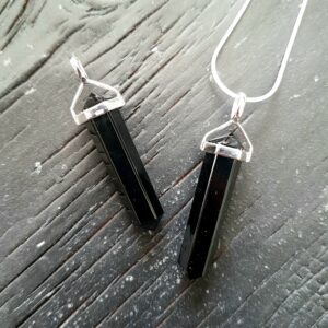 Two Black Agate Double Terminated points (black faceted points at both ends), on a silver chain, on a dark wooden board