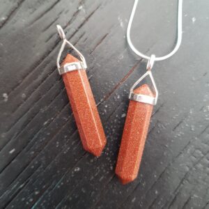 Two Brown Goldstone Double Terminated points (brown with copper flecks faceted with points at both ends), on a silver chain, on a dark wooden board