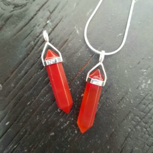Two Carnelian Double Terminated points (deep red faceted points at both ends), on a silver chain, on a dark wooden board