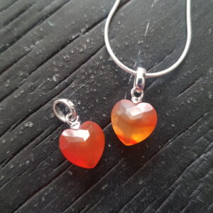 Two Carnelian heart pendants - orange stone cut into a faceted shape on a silver chain - on a dark wooden board